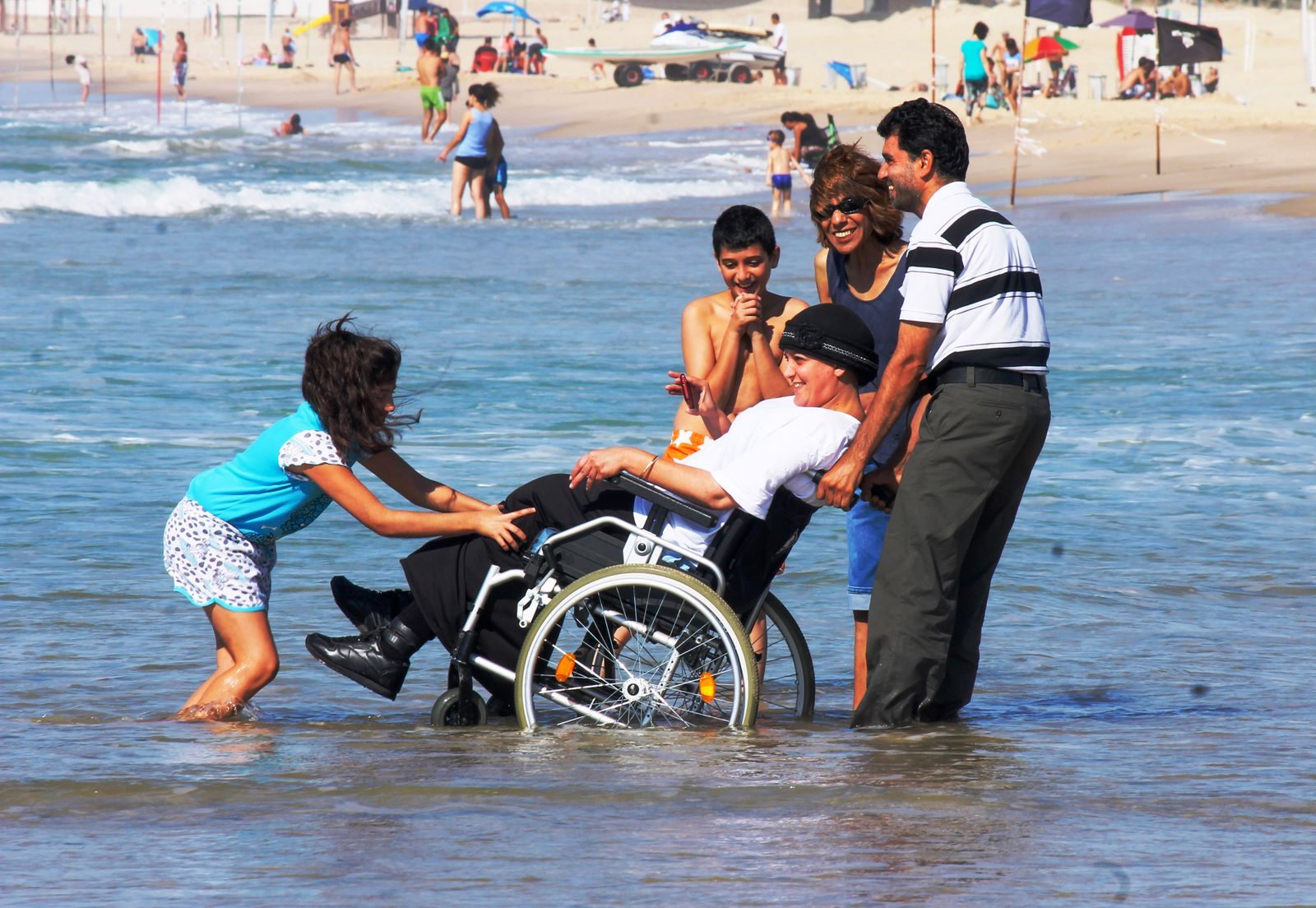 Family helping a wheelchair user into the surf